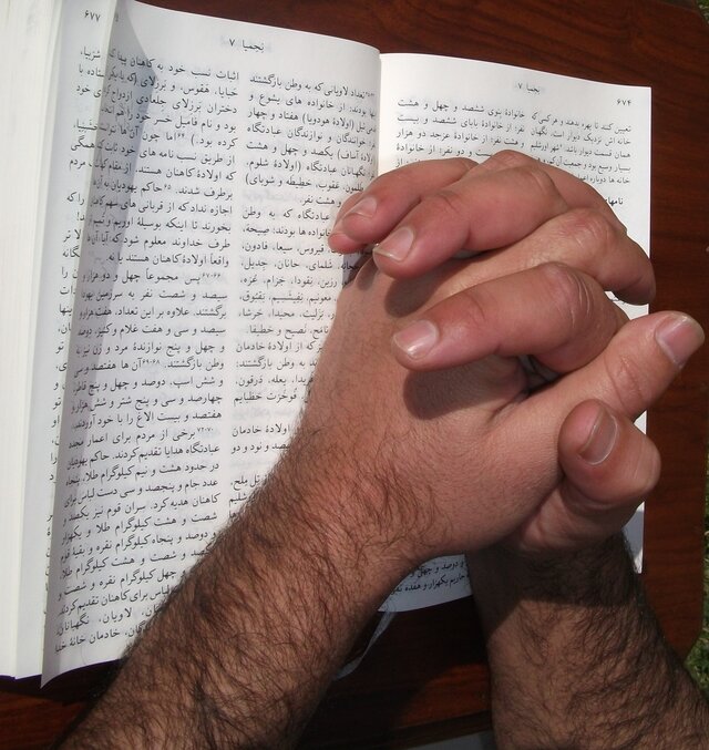 دست‌هایی که در دعا بر روی کتاب مقدس بازِ دری به هم گره خورده‌اند